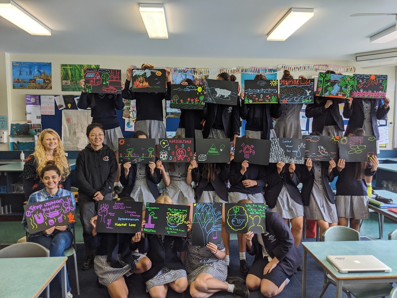 Monash University’s Yvonne Hora and Boer Tan (standing) and The University of Melbourne’s Eliza Rokhsat (seated) with students from Melbourne Girls College with their artworks about what inspires them to learn more about environmental science.